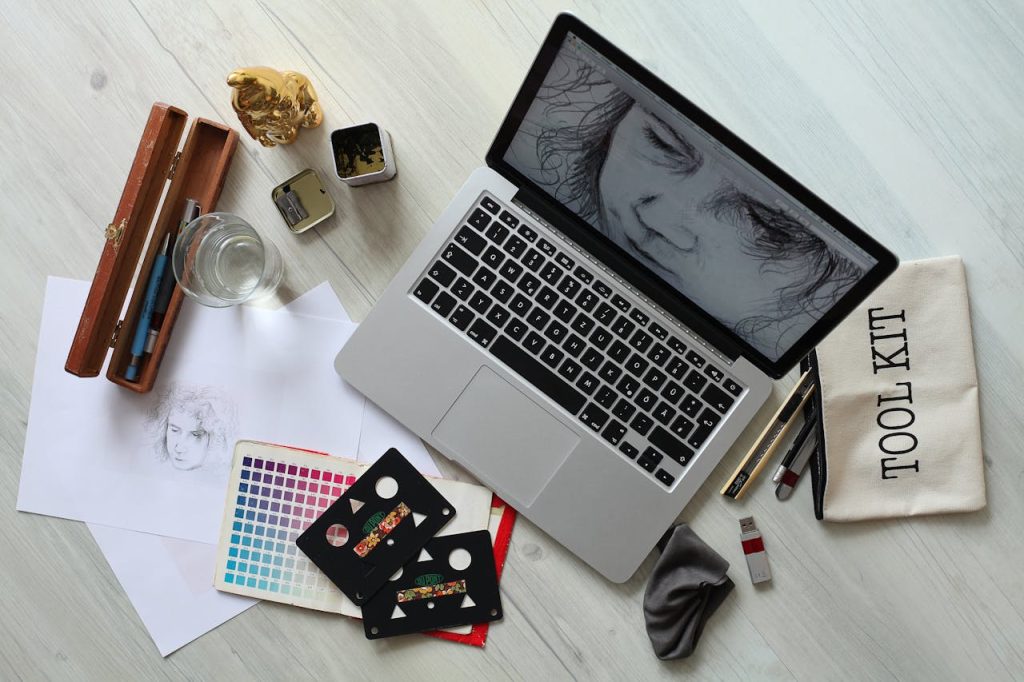 Top view of a creative workspace with a laptop, sketch supplies, and color palette.